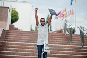 African student male posed with backpack and school items on yard of university, against flags of different countries. photo