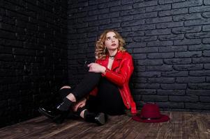 Studio portrait of blonde girl with red hat and leather jacket posed against brick wall. photo