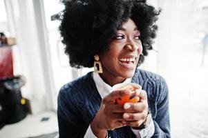 Curly hair african american woman wear on sweater posed at cafe indoor with cup of tea or coffee. photo