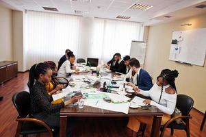 Multiracial business team addressing meeting around boardroom table, working together and write something on papers. photo