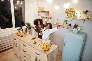 Two african american female friends women spending time at kitchen with wine. Black girlfriends  relaxing at home. photo