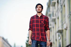 Young indian student man at red checkered shirt and jeans walking at city. photo