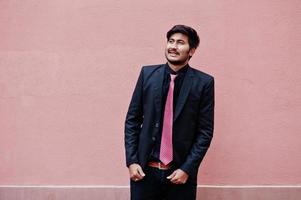 Young indian man on suit and tie posed against pink wall. photo