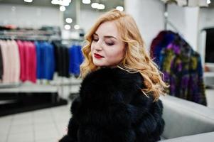 Elegance blonde girl in fur coat at the store of fur coats and leather jackets. photo