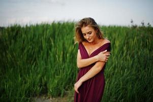 Blonde sensual woman in red marsala dress posing in the reeds. photo