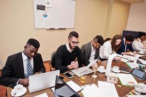 Multiracial business team addressing meeting around boardroom table, working together and write something on papers. photo