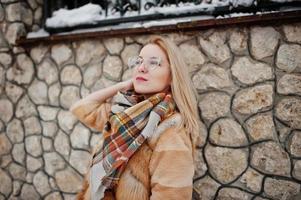 retrato de chica rubia con gafas, abrigo de piel rojo y bufanda en el día de invierno. foto