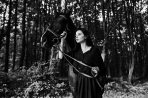 Mystical girl wear in black with horse in wood. photo
