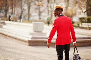 Back of fashion african american man model at red suit, with highlights hair and handbag posed at street. photo