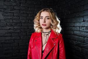 retrato de estudio de una chica rubia con una chaqueta de cuero roja contra una pared de ladrillos. foto