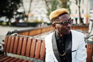 Chic handsome african american man in white suit and sunglasses sitting on bench. photo