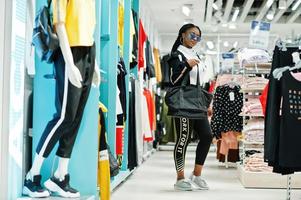 Afican american women in tracksuits and sunglasses shopping at sportswear mall with sport bag against shelves. Sport store theme. photo