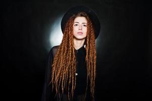 Studio shoot of girl in black with dreads and hat at black background. photo