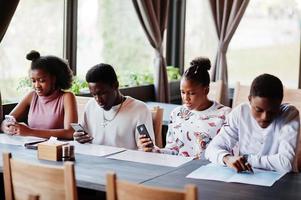 Happy african friends sitting and chatting in cafe. Group of black peoples meeting in restaurant and look at their mobile phone. photo