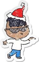 distressed sticker cartoon of a boy wearing sunglasses pointing wearing santa hat vector