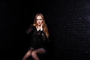 Studio shot of brunette girl in black blouse with bra and shorts against black brick wall. photo
