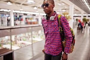 African american man in checkered shirt, sunglasses and jeans with suitcase and backpack. Black man traveler on duty free. photo