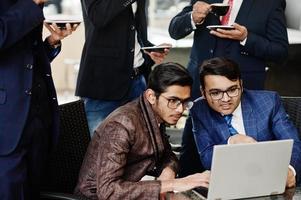 grupo de cinco hombres de negocios indios en trajes sentados en la oficina en el café mirando la computadora portátil y tomando café. foto