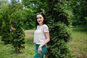 Brunette girl in green skirt and white blouse posed at park. photo