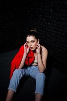 chica morena con estilo en chaqueta roja contra la pared de ladrillo negro de estudio. foto