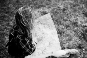 Portrait of a positive young gorgeous blonde sitting on the ground with a map in her hands in the forest. photo