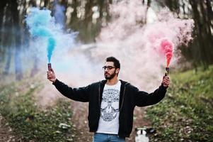 Street style arab man in eyeglasses hold hand flare with red and blue smoke grenade bomb. photo