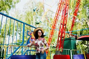 retrato de una chica morena con gafas rosas y sombrero con helado en el parque de atracciones. foto