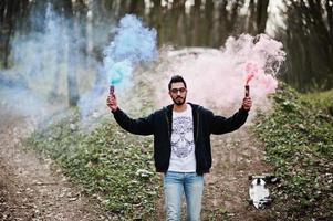 Street style arab man in eyeglasses hold hand flare with red and blue smoke grenade bomb. photo