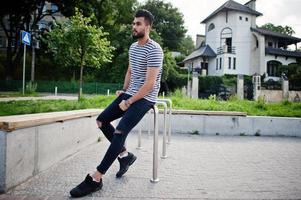 Handsome tall arabian beard man model at stripped shirt posed outdoor. Fashionable arab guy. photo