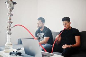 Two handsome and fashionable indian mans relaxing at room and smoking hookah. photo