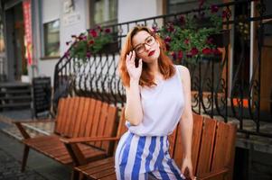 atractiva mujer pelirroja con anteojos posando en la calle de la ciudad de la primavera. foto