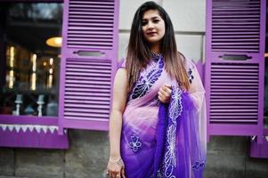 Indian hindu girl at traditional violet saree posed at street against purple windows. photo