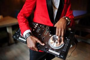 manos de moda hombre afroamericano modelo dj en traje rojo con controlador de dj. foto