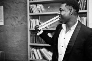 Strong powerful african american man in black suit against book shelves in free books anti cafe. photo