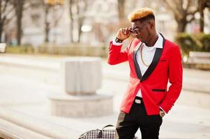 modelo de hombre afroamericano de moda en traje rojo, con cabello destacado y bolso posado en la calle. foto