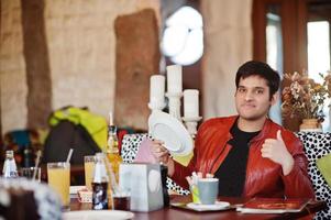 hombre indio elegante con ropa informal sentado en un café interior y sosteniendo un plato en las manos. foto