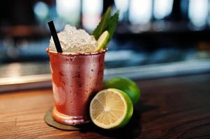 cóctel alcohólico con hielo y limón en lata de bronce en la mesa del bar. foto