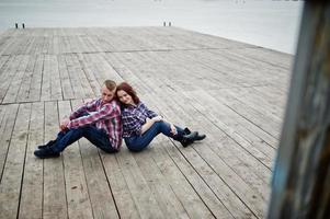 Stylish couple wear on checkered shirt in love together sitting on pier. photo