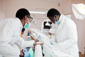 tres médicos afroamericanos trabajando con una laptop, discutiendo con colegas en la clínica dental. foto