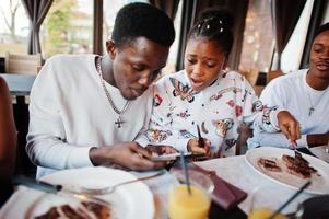 Happy african friends sitting, chatting in cafe and eat food. Group of black peoples meeting in restaurant and have dinner. Surprised face when seen guest check. photo