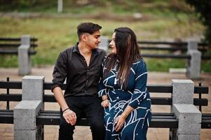 Love story of indian couple posed outdoor, sitting on bench together. photo