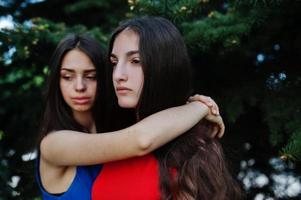 Two teenagers girl in blue and red dresses posed outdoor and hugging. photo