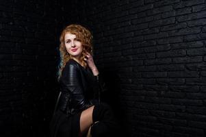 Curly hair girl at leather jacket on studio against black brick wall. photo