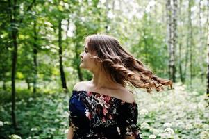 Portrait of a fabulous young girl in pretty dress with stylish curly hairstyle posing in the forest or park. photo