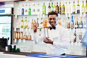 camarero afroamericano en el bar con agitador. preparación de bebidas alcohólicas. foto