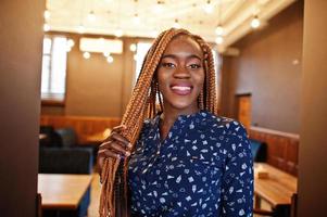 Portrait of beautiful young african business woman, wear on blue blouse and skirt, posing in cafe. photo