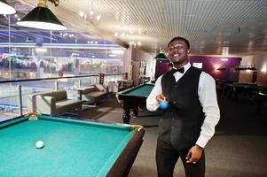 Young handsome african man wearing white shirt, black vest and bow tie play pool billiard. photo