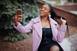 Young stylish beautiful african american woman in street, wearing fashion outfit coat, with mobile phone. photo