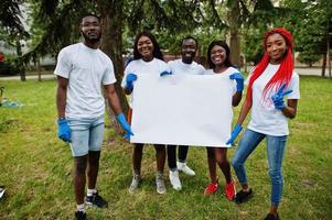 un grupo de voluntarios africanos felices sostiene un tablero en blanco vacío en el parque. Concepto de voluntariado, caridad, personas y ecología de África. espacio libre para su texto. foto