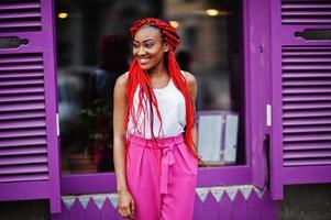 chica afroamericana de moda en pantalones rosas y rastas rojas posadas al aire libre. foto